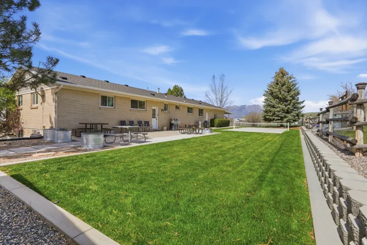 Expansive backyard with a manicured lawn, concrete patio, and a dedicated volleyball court