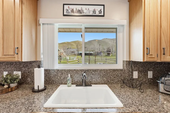 White single-basin sink with a stainless steel faucet, granite-finish countertops, and light wood cabinetry