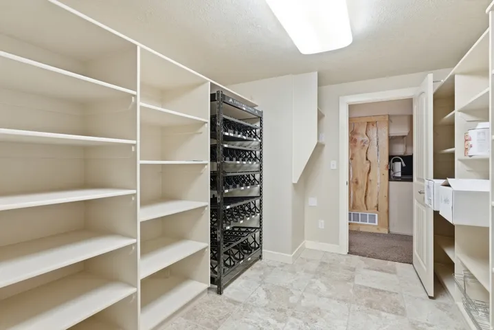 Spacious storage room featuring extensive built-in shelving, a dedicated wine rack, and durable tile flooring