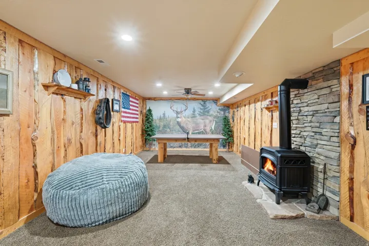 Recessed lighting, wood plank wall finishes, stone accent wall, ceiling fan, and wood-burning stove