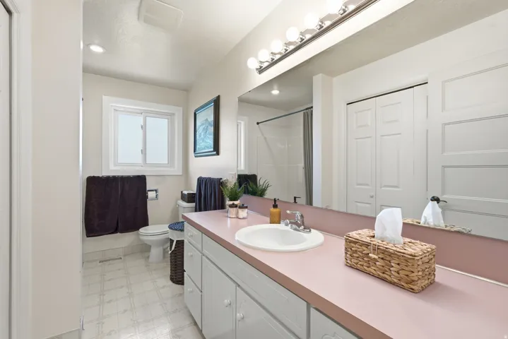 Bathroom featuring a single vanity with an integrated sink, wall-mounted mirror, overhead vanity lighting, and a sliding window