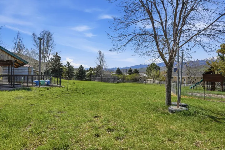 Expansive grassy yard with mature trees and mountain scenery