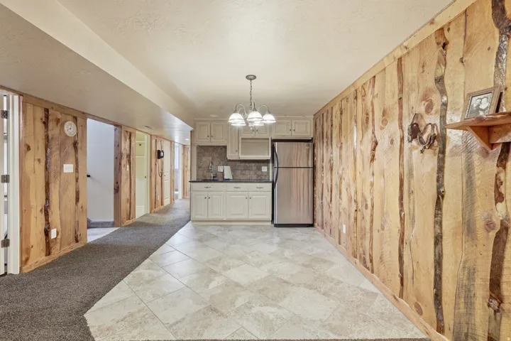Wood-paneled wall, white cabinetry, stainless steel refrigerator, tile flooring, and a multi-light chandelier