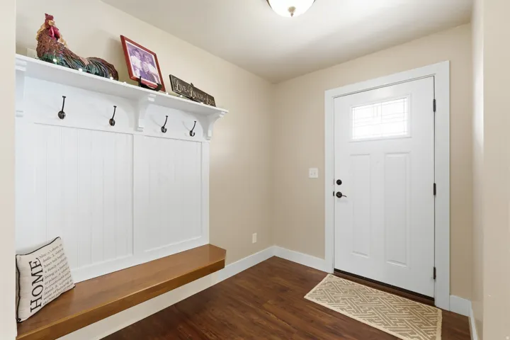 Built-in storage bench with wood surface, white paneling, and four coat hooks