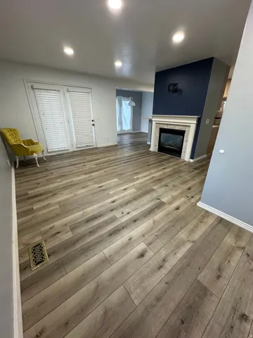 Wood-finish flooring throughout, recessed lighting, and a modern fireplace with a white mantel and stone surround