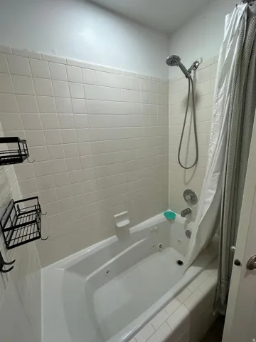 White tile surround, built-in jetted tub, wall-mounted showerhead, and chrome fixtures