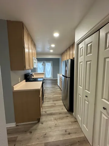 Galley kitchen featuring wood-finish flooring, recessed lighting, light-toned cabinetry, and stainless steel appliances