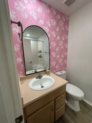 Vanity with an integrated sink and light wood-finish cabinetry, complemented by an arched mirror and patterned wall covering