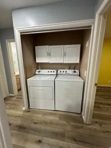 Dedicated laundry closet featuring white upper cabinetry and wood-finish flooring