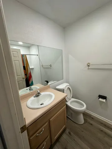 Bathroom featuring a wood-finish vanity with an integrated sink, a large wall-mounted mirror, and wood-finish flooring