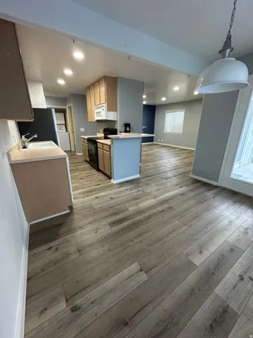Wood-finish flooring throughout, kitchen with light wood cabinetry, black appliances, and white microwave
