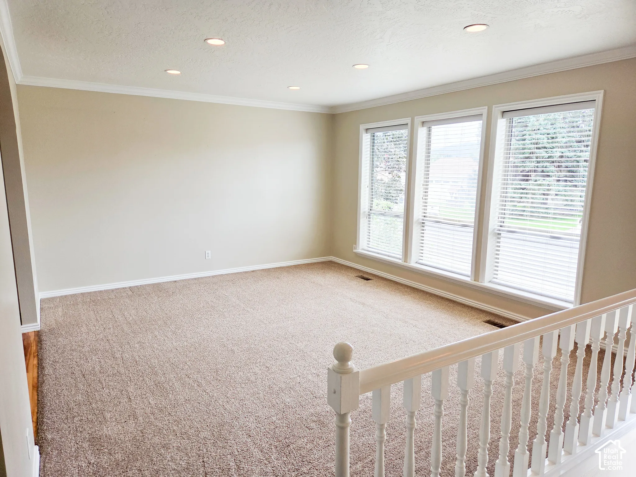 Recessed lighting, crown molding, three windows, light-colored carpet, and a white wood-finish railing
