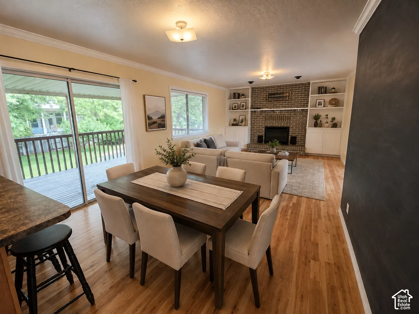 Wood-finish flooring, built-in shelving, brick fireplace, crown molding, and sliding glass door with deck access