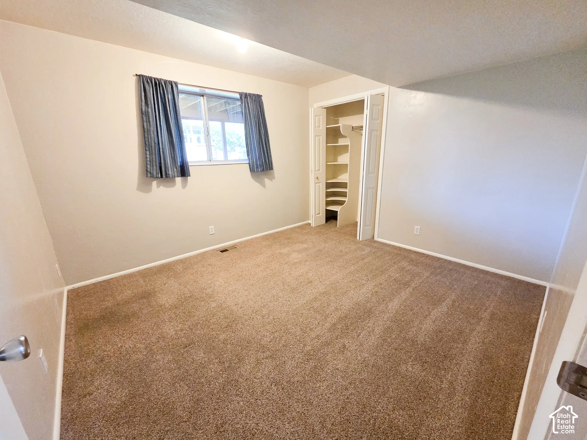 Neutral-toned walls with a window, brown carpeting, and a built-in closet with shelving