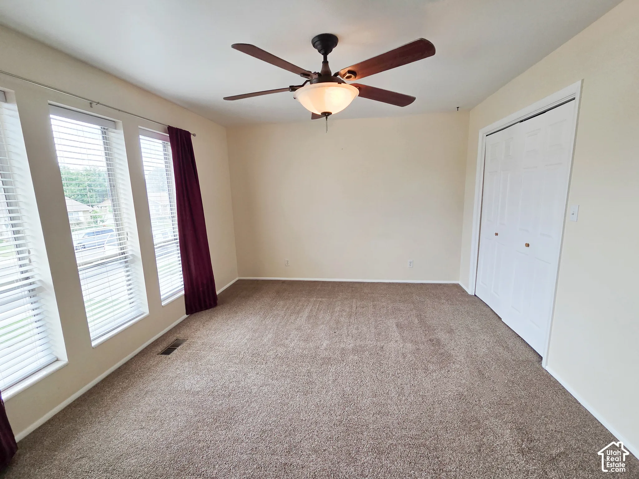 Room featuring a ceiling fan with integrated lighting, multiple windows with blinds, and neutral carpeting