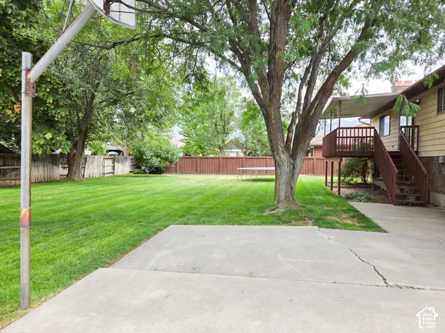 Expansive green lawn, mature trees, concrete patio, wooden privacy fencing, and a raised wooden deck with stairs