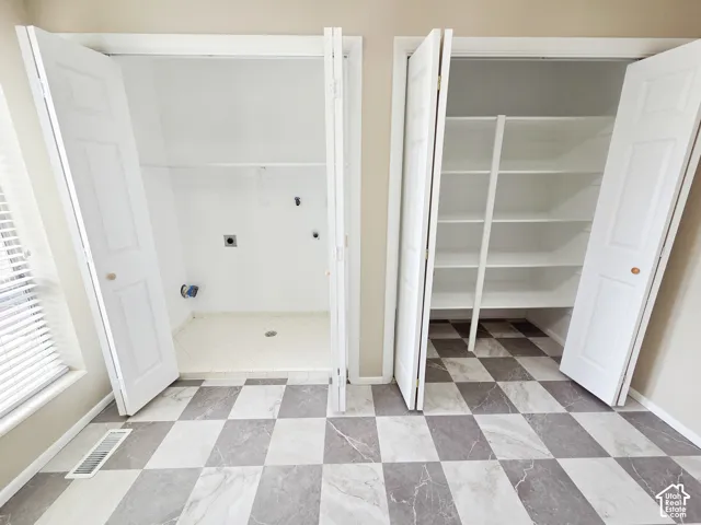 Dedicated laundry closet with tile flooring, bifold doors, and an adjacent storage closet with built-in shelving