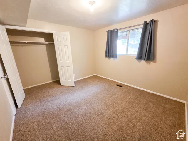 Carpeted room featuring a window with a curtain rod, a ceiling-mounted light fixture, and a built-in closet with bi-fold doors and a hanging rod