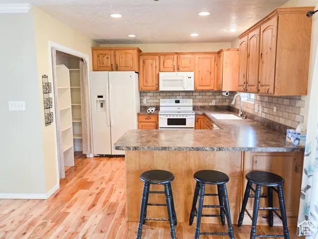 Kitchen featuring wood-finish cabinetry, solid surface countertops, white appliances, subway tile backsplash, and wood-finish flooring