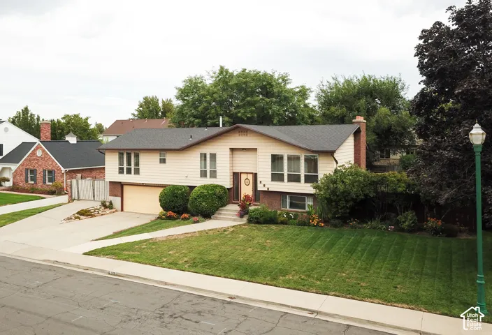 Split-level residence featuring a two-car garage, brick chimney, and a concrete driveway