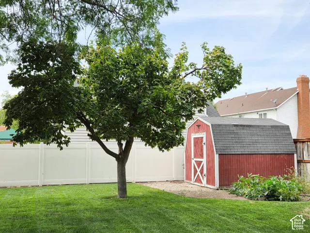 Expansive backyard featuring a manicured lawn, established tree, white vinyl fencing, and a red storage shed with a gambrel roof