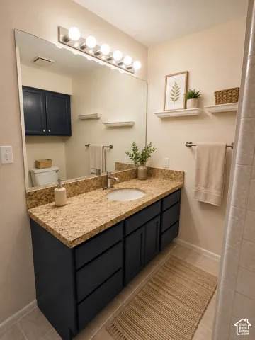 Dual-sink vanity featuring a stone countertop, dark cabinetry, and a full-width mirror with overhead lighting