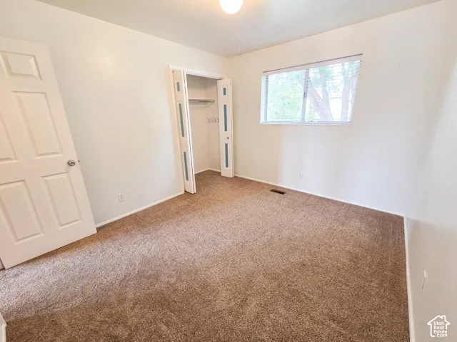Wall-to-wall carpeting, window with horizontal blinds, built-in closet with bifold doors, and a ceiling-mounted light fixture