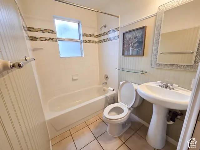 White subway tile surround with decorative accent band, pedestal sink, ceramic tile flooring, and frosted window