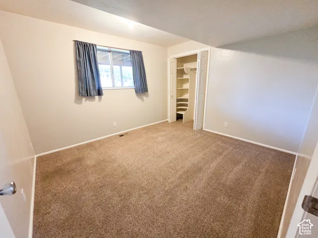 Neutral-toned walls with a window, brown carpeting, and a built-in closet with shelving