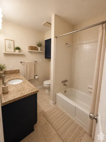 Bathroom featuring a single vanity with a white basin and speckled countertop, a white bathtub with a tiled surround, and ceramic tile flooring