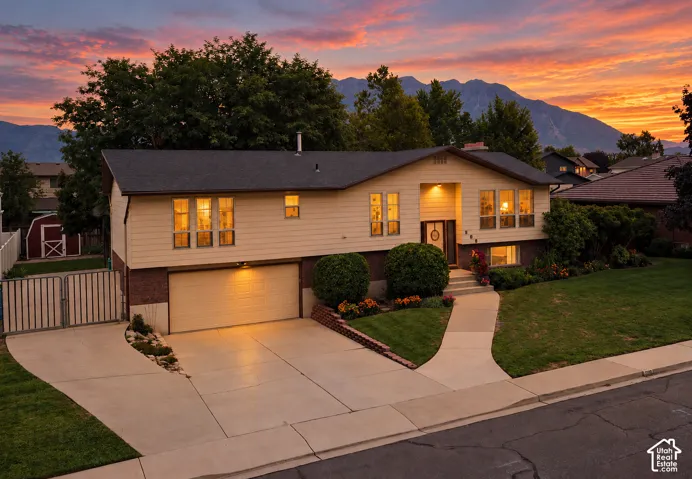 Split-level residence featuring a two-car garage, concrete driveway, front yard landscaping, and a red shed