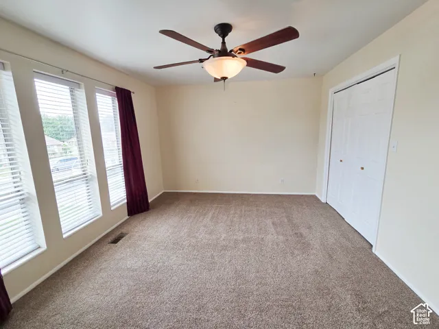 Room featuring a ceiling fan with integrated lighting, multiple windows with blinds, and neutral carpeting