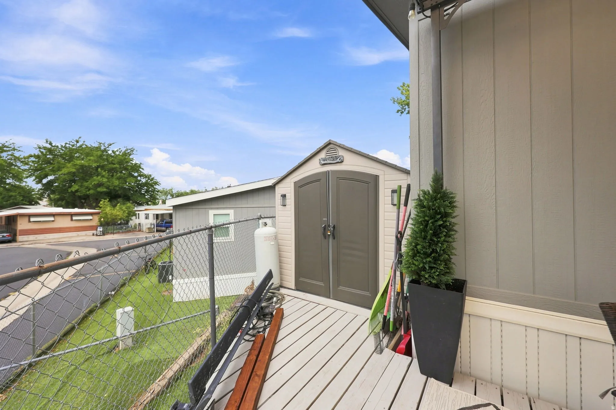 Deck with wood-finish flooring, featuring a storage shed with dual doors and a chain-link fence