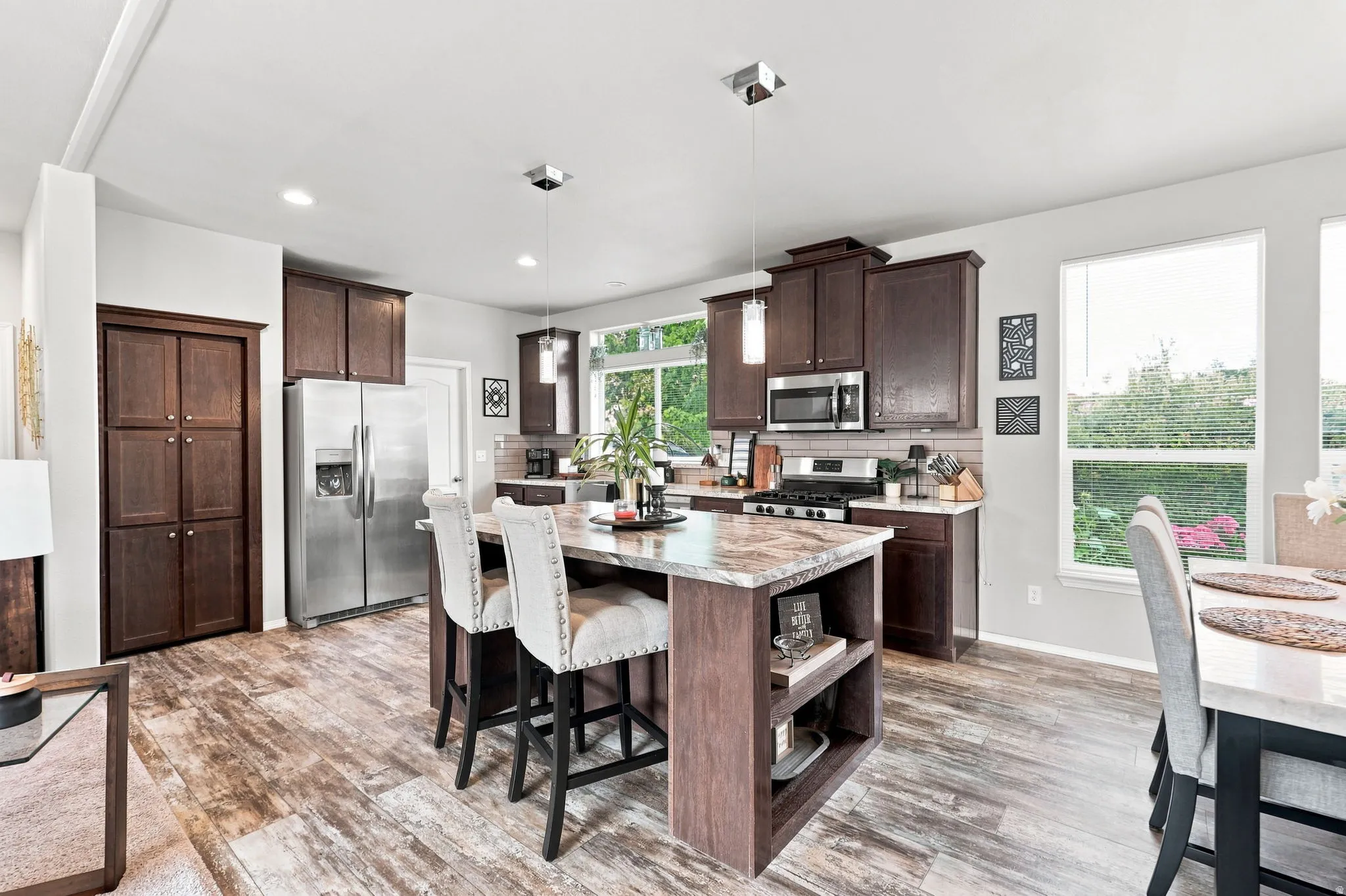 Kitchen featuring wood-finish flooring, dark wood cabinetry, a center island with a stone countertop, stainless steel appliances, and recessed lighting