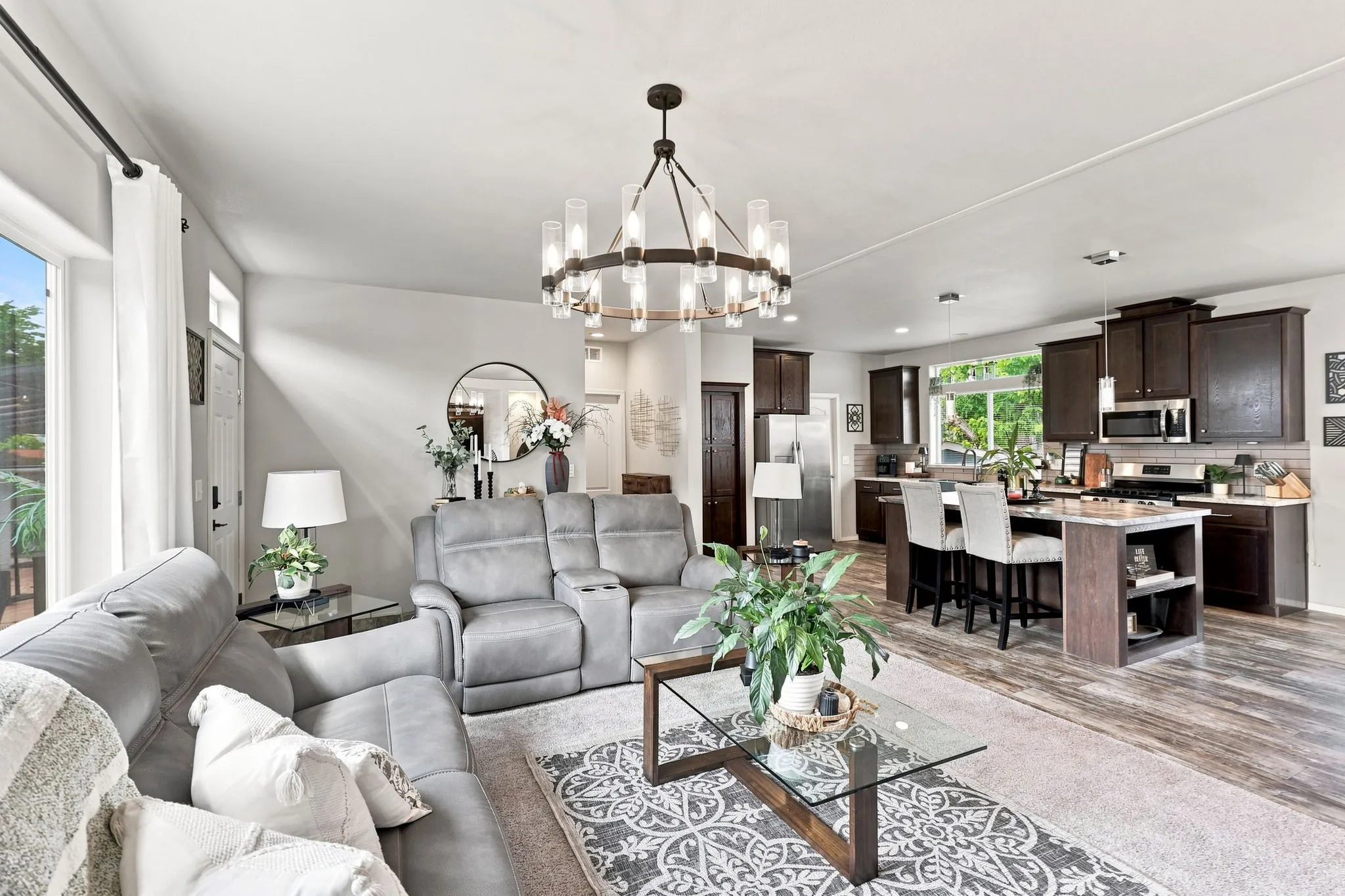 Open-concept living space featuring wood-finish flooring, a contemporary chandelier, dark wood cabinetry, a kitchen island with seating, and a stainless steel appliance suite