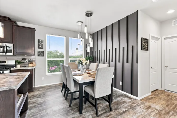 Wood-finish flooring throughout, with a decorative accent wall and a multi-pendant light fixture over the dining area