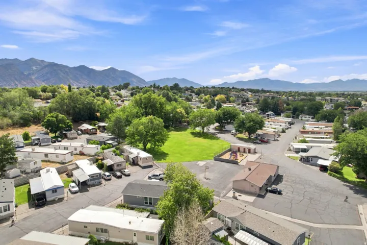 Expansive green common area, paved roadways, mountainous backdrop, and mature trees