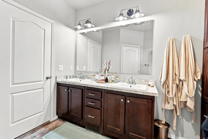 Dual sink vanity with dark wood-finish cabinetry, light-colored countertops, and a large wall-mounted mirror