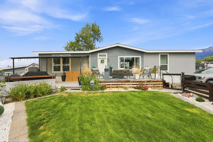 Modern manufactured home featuring a spacious rear yard with manicured lawn, mature landscaping, and decorative hardscaping