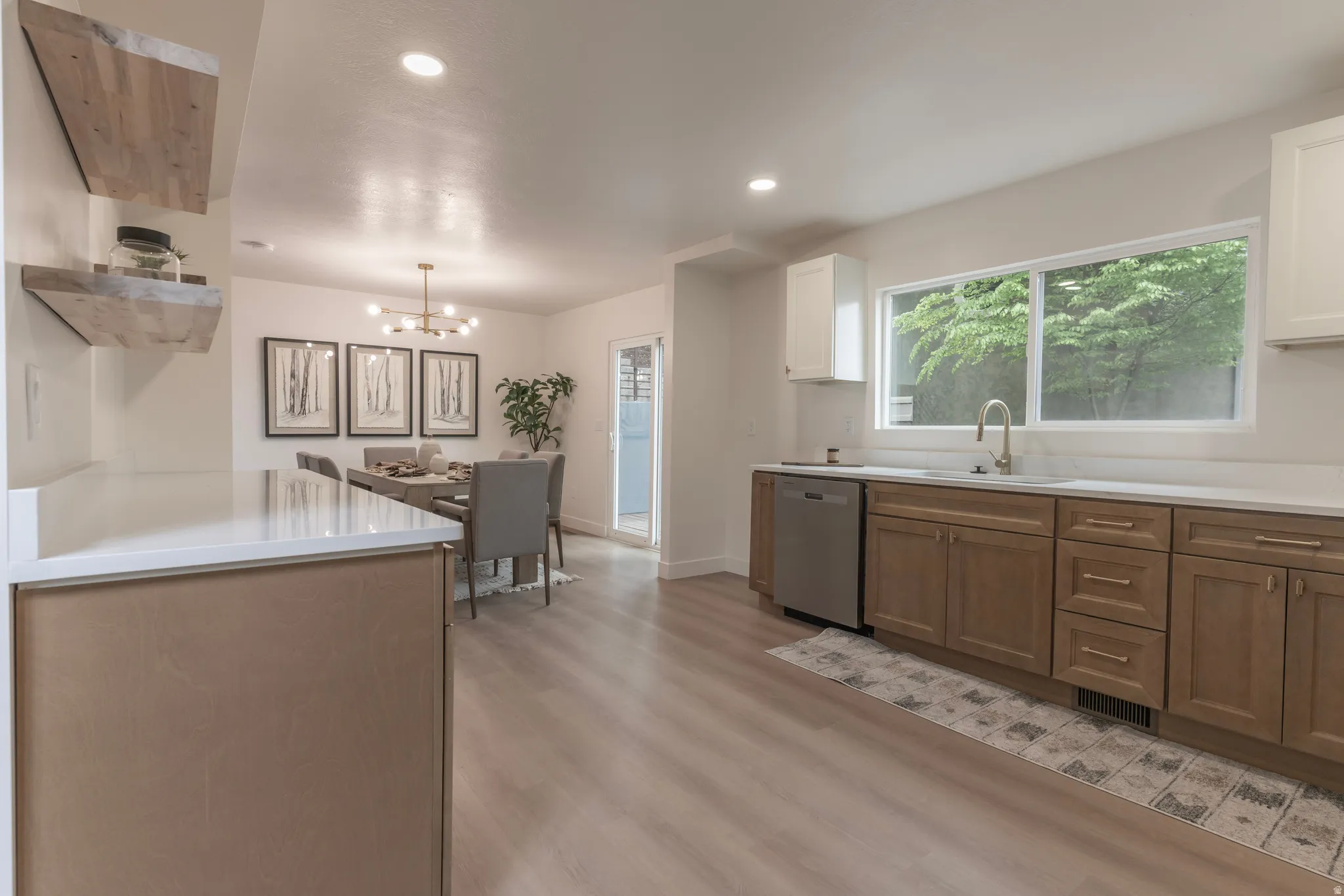 Kitchen with wood-finish flooring, white countertops, a stainless steel dishwasher, and a single basin sink with a gooseneck faucet