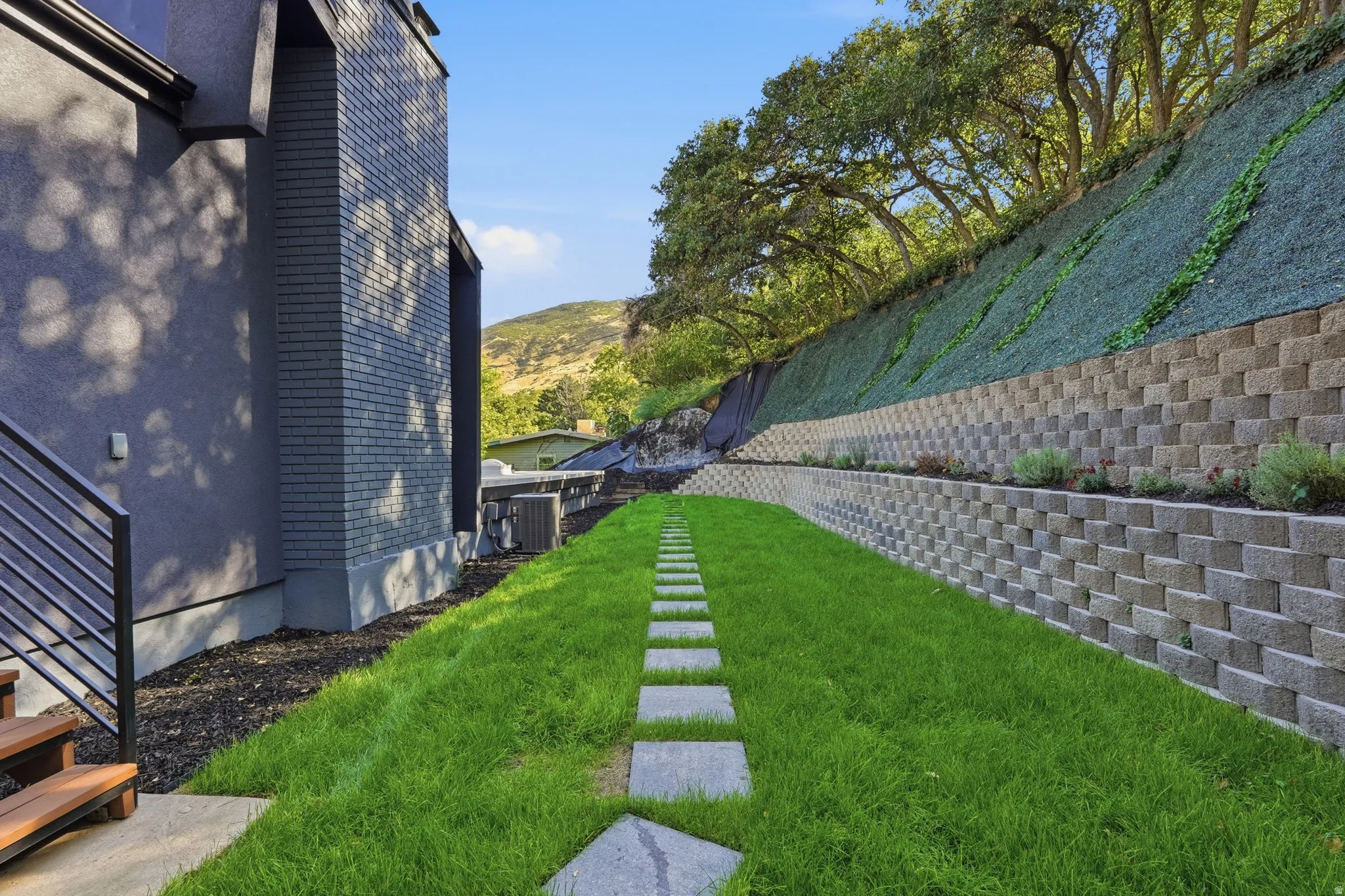 Manicured lawn with stepping stones, tiered retaining walls, and established upper-level landscaping