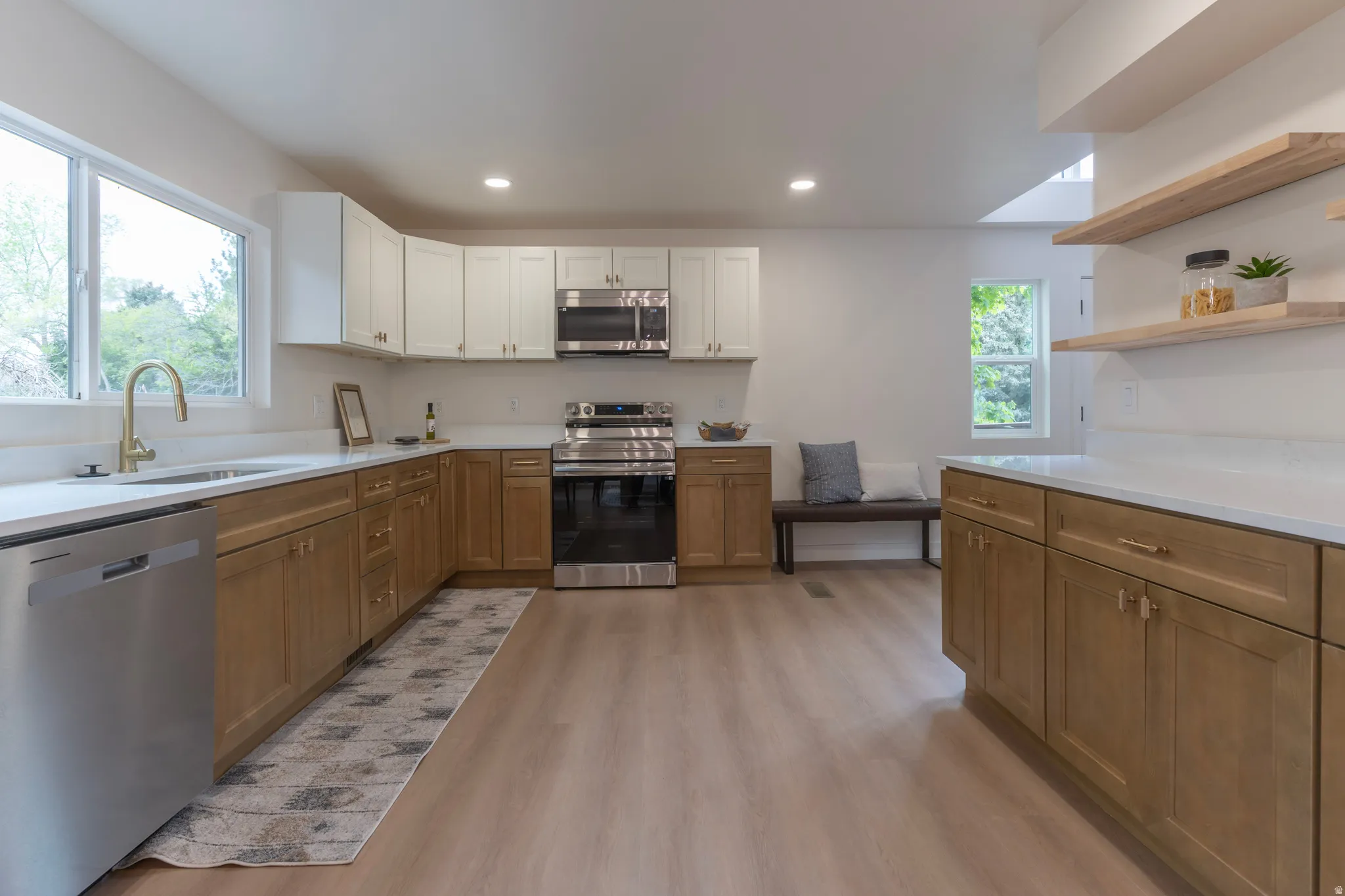 Modern kitchen featuring light wood-finish flooring, two-tone cabinetry, stainless steel appliances, white countertops, and a gold-finish faucet