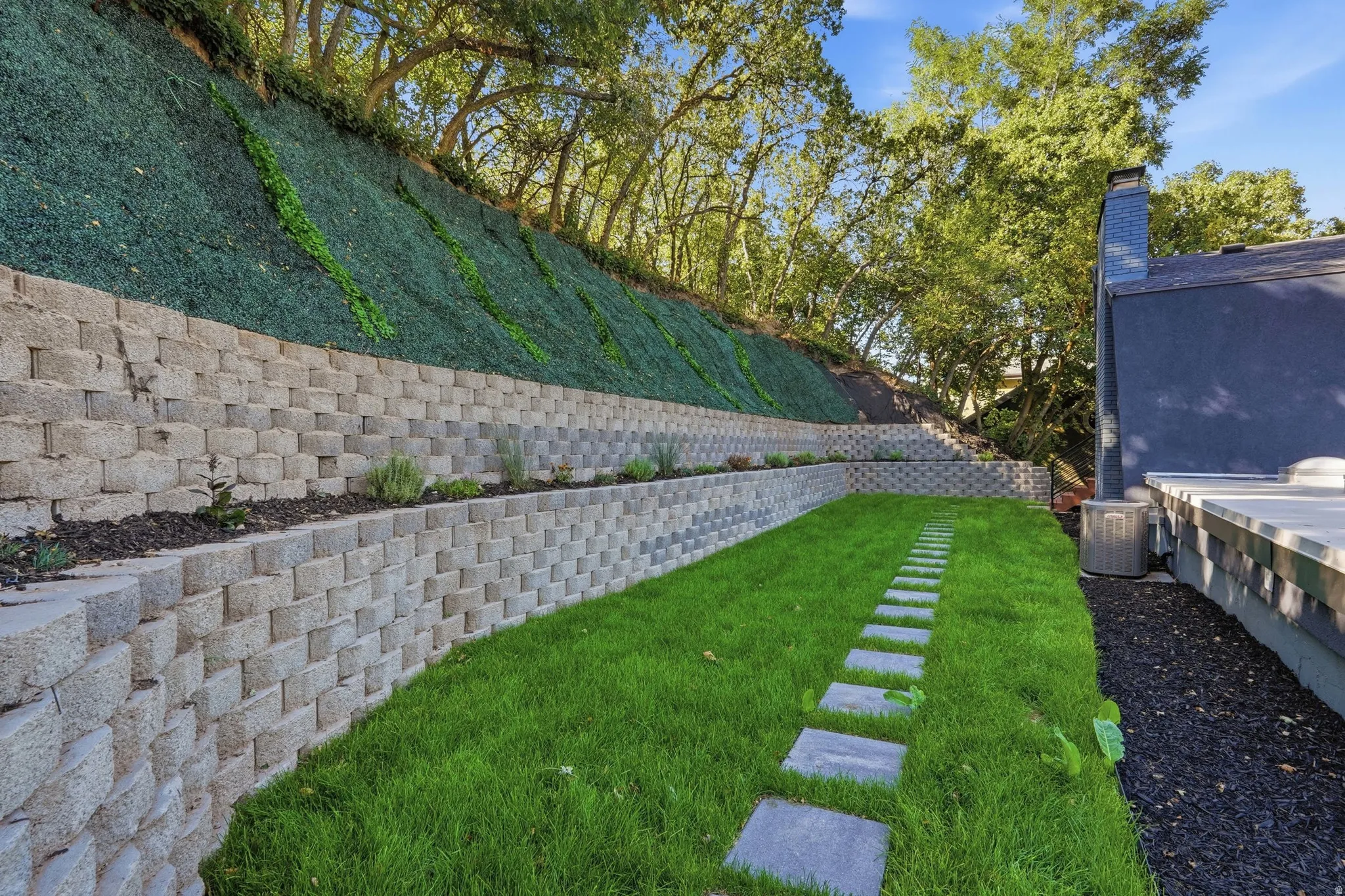 Tiered retaining walls with integrated planting beds, established ground cover, and mature trees