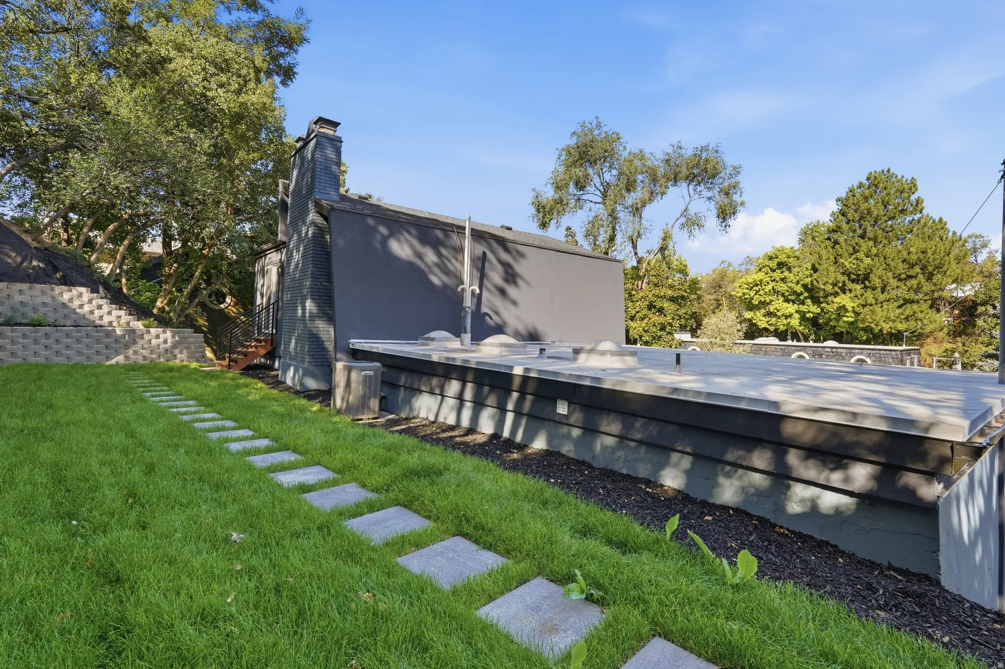 Expansive green lawn with stepping stone pathway, tiered retaining wall, and a rooftop deck
