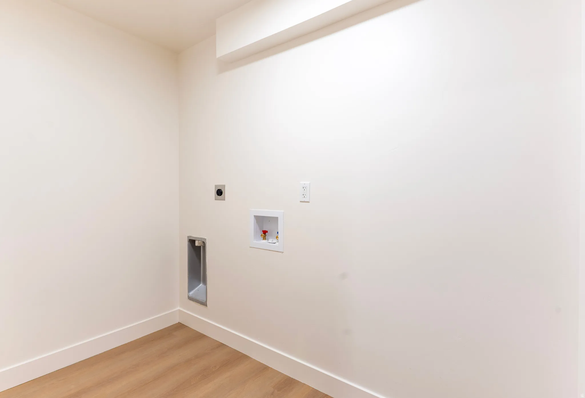 Laundry hookups with wood-finish flooring and neutral wall tones