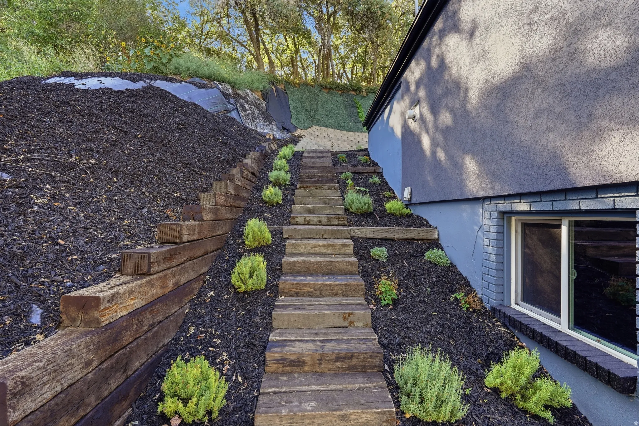 Terraced landscaping featuring wood-tie retaining walls, a wood-finish staircase, and low-maintenance plantings