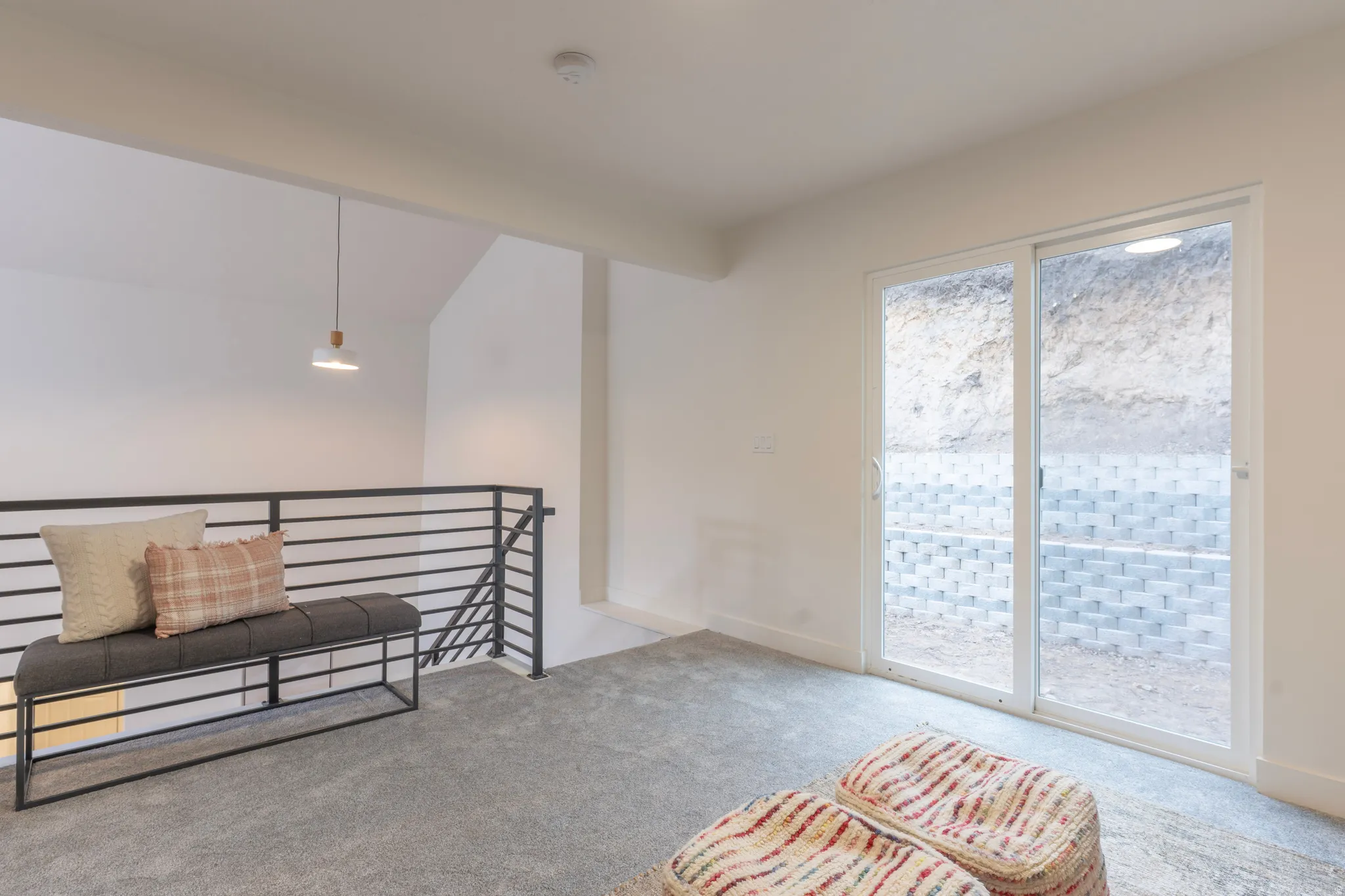 Sliding glass door, horizontal slat railing, wood-finish pendant light fixture, and light-colored carpeting