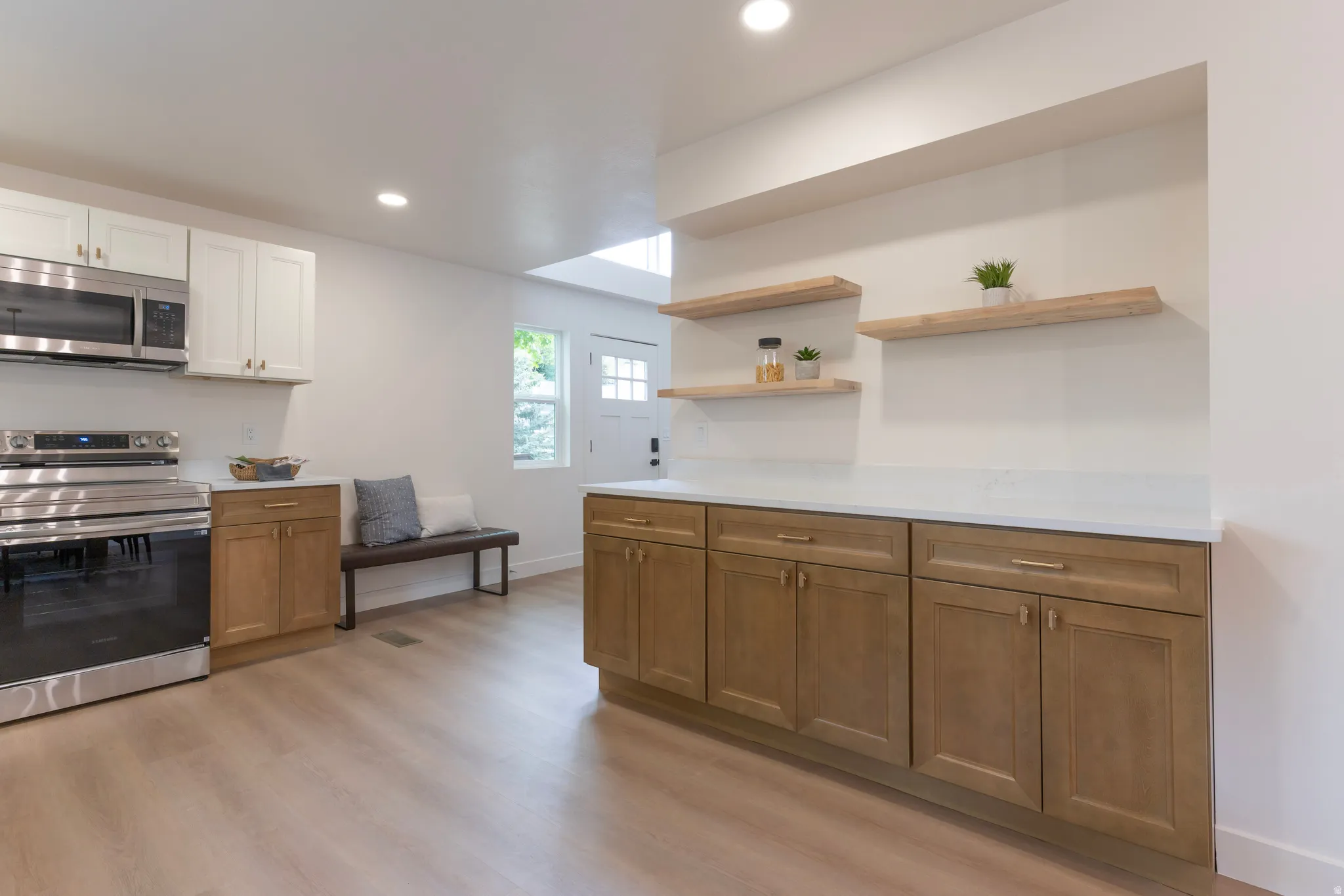 Modern kitchen featuring stainless steel appliances, wood-finish flooring, white upper cabinetry, and natural wood lower cabinetry