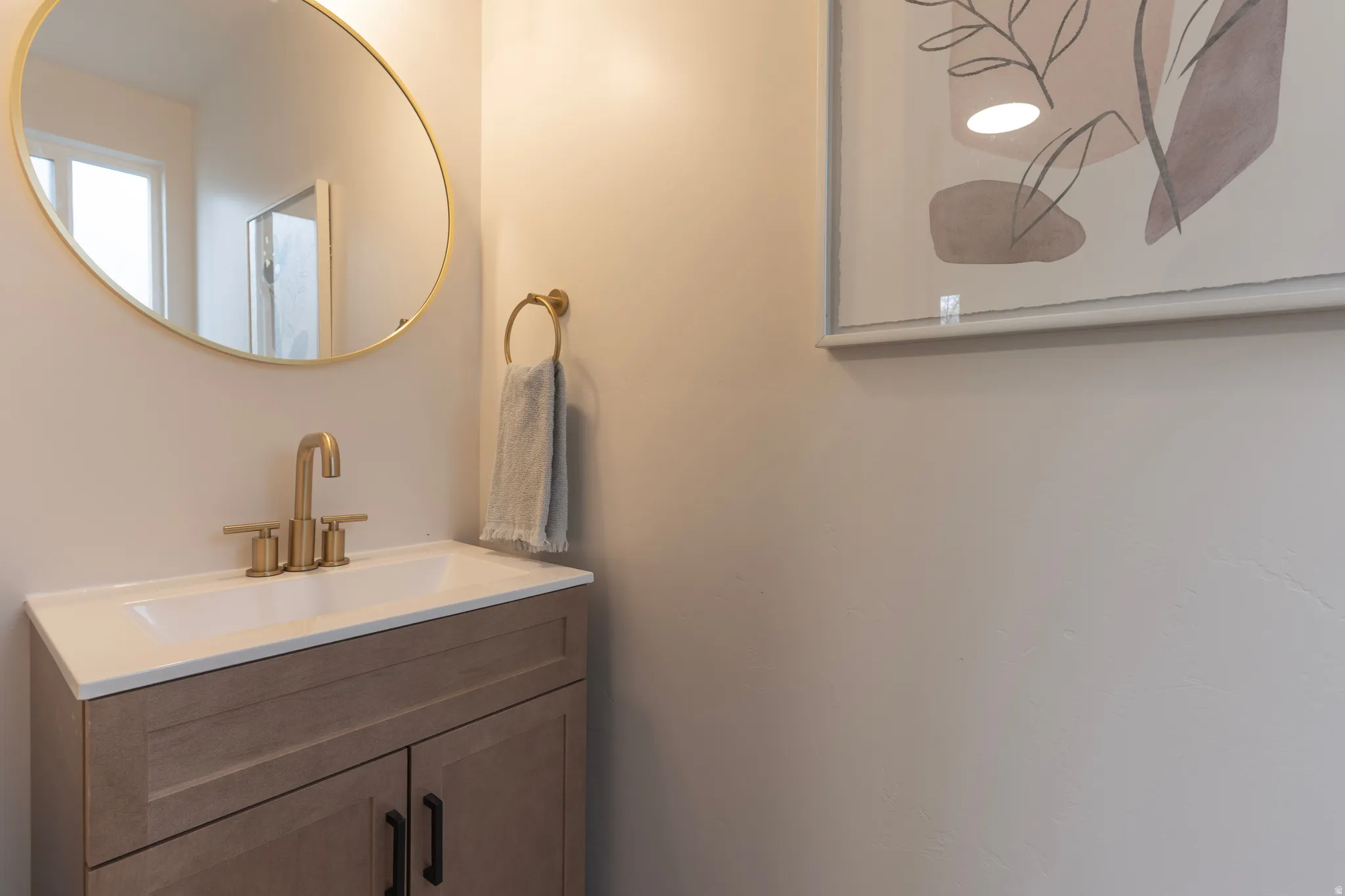 Recessed sink with a bronze-finish faucet, wood-finish vanity with dark hardware, and a circular mirror with a bronze-finish frame
