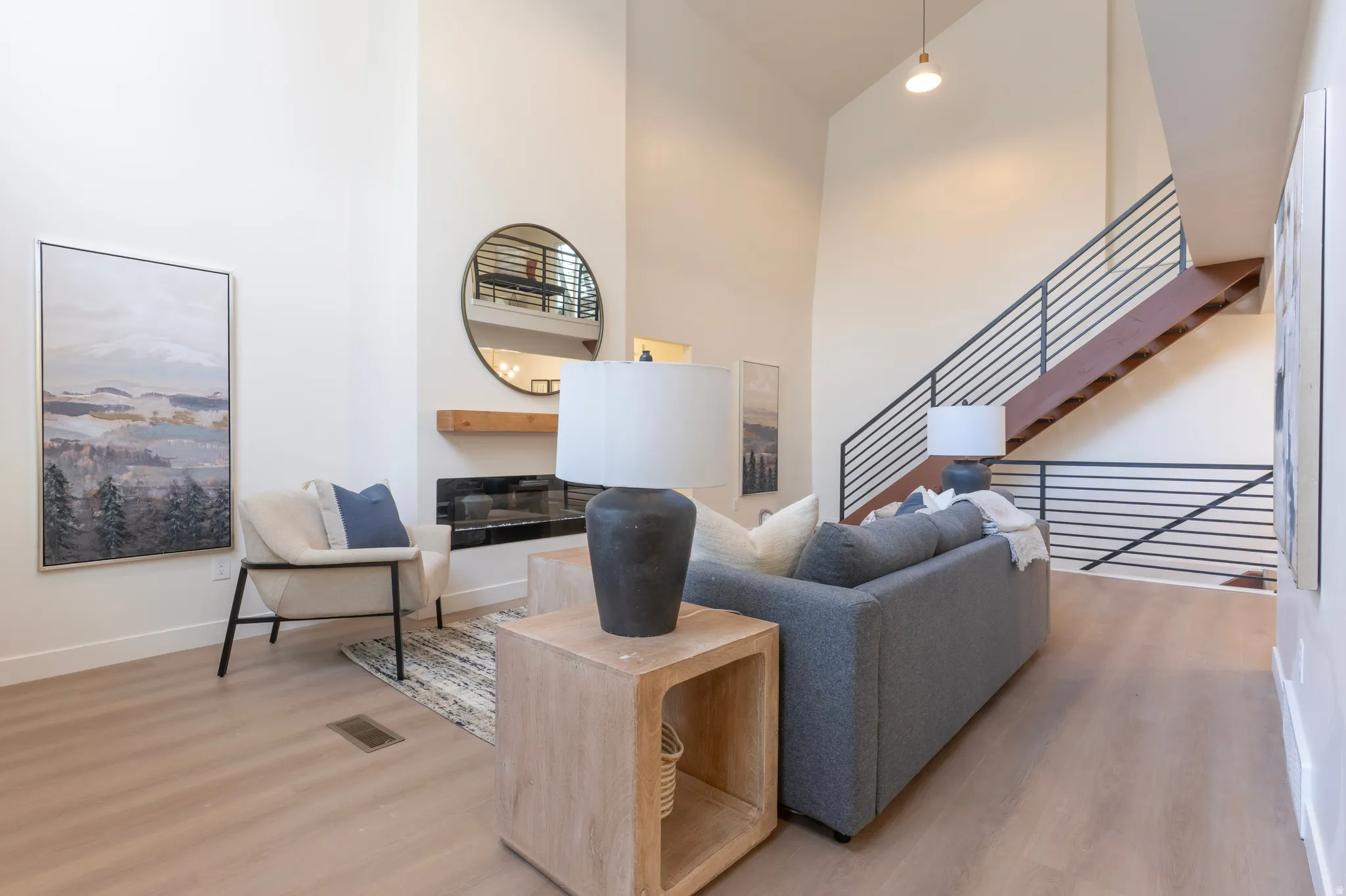 Vaulted ceilings, wood-finish flooring, linear fireplace with a wood mantle, and an open-tread staircase with horizontal railings